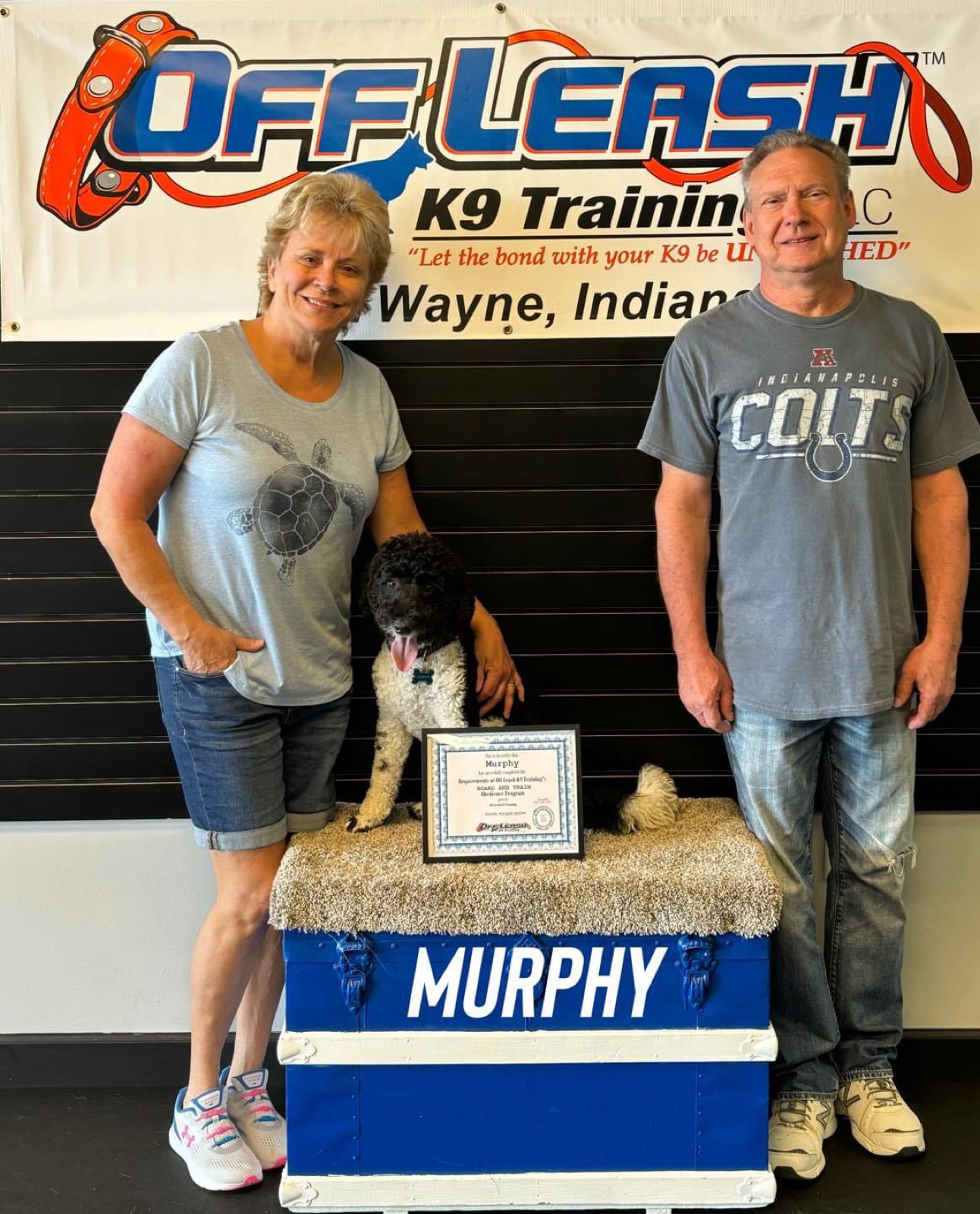Murphy with his family and his certificate in front of the Off Leash K9 Training Fort Wayne banner